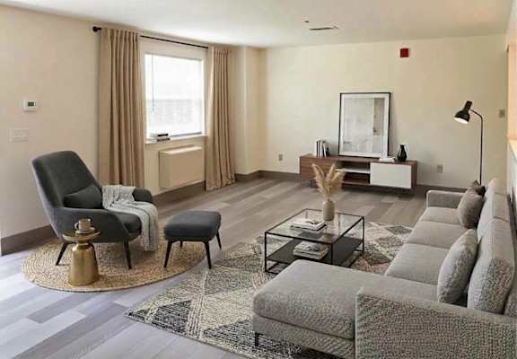 A living room with a grey sofa, a black chair, and a glass coffee table.