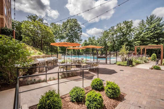 A patio with a pool and a table surrounded by bushes.