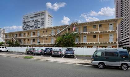 A street view with cars parked on the side and apartment buildings in the background.