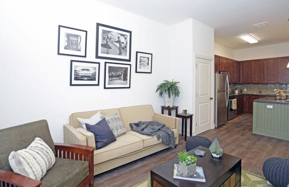 Living room with open layout, hardwood floors and view of kitchen; model pictured with gallery wall, coffee table and couches