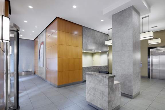 A modern office lobby with a reception desk and a large marble pillar at The Ellington Apartments, New York, NY, 10019