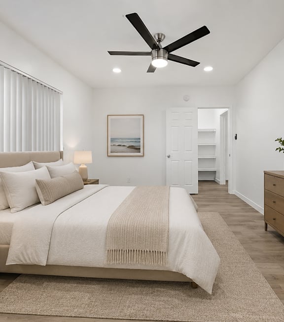 A bedroom with a large bed, a ceiling fan, and a wooden dresser.