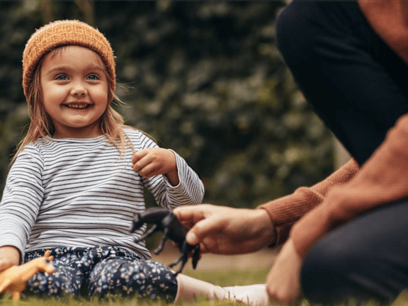 a little girl sitting on the grass next to her parent