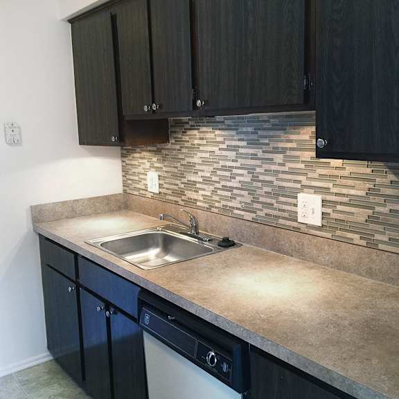 A kitchen with a stone backsplash and dark cabinets.