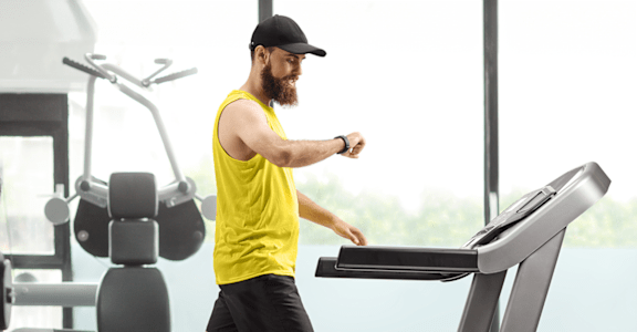 A man in a yellow shirt and black shorts is running on a treadmill in a gym.