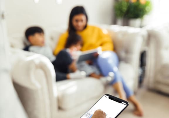 a man holding a cell phone in a living room with a family on the couch