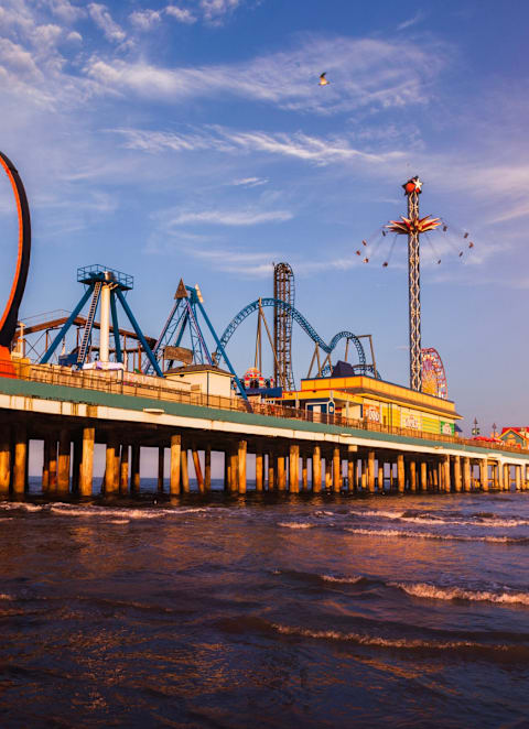 A pier with a large orange roller coaster and other amusement rides.