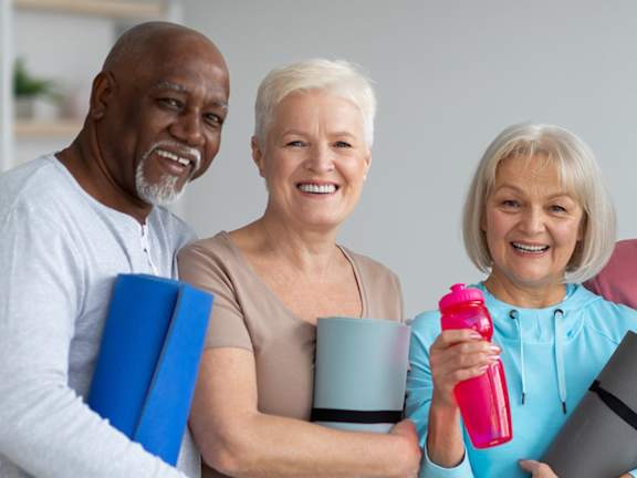 Three people holding yoga mats and water bottles.