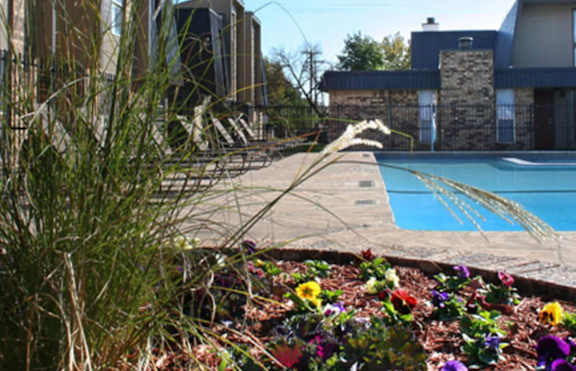 A pool surrounded by a flower bed and a building in the background.