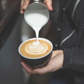 a person pouring milk into a cup of coffee