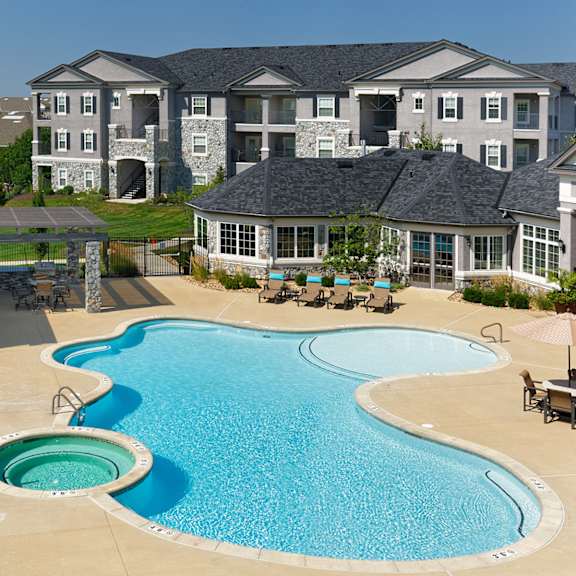 a large swimming pool with lounge chairs and a hot tub in front of an apartment building