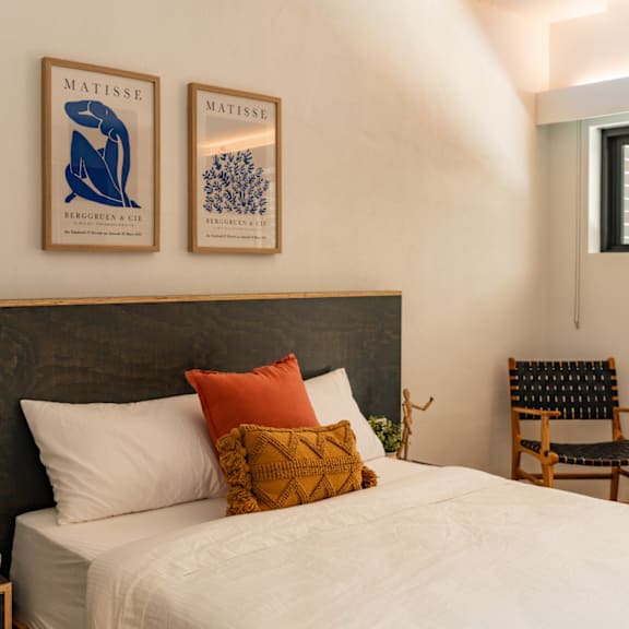 A bedroom with a bed, two pillows, a chair, and two framed pictures on the wall.