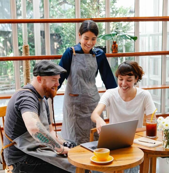 Three people are working on a laptop in a cafe.