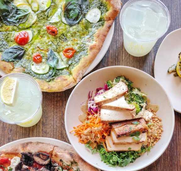 A variety of pizzas and salads are displayed on a wooden table.