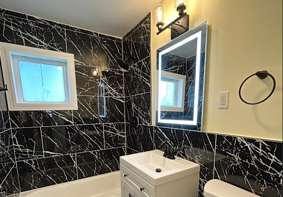 A white toilet sits in a bathroom with black marble tiles.
