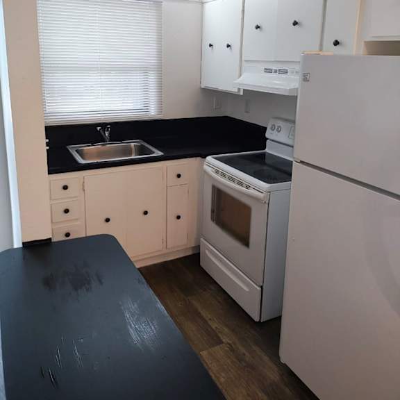 A kitchen with white appliances and black countertops.