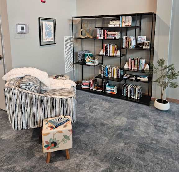 A room with a bookshelf, a chair, and a small tree.