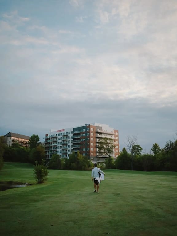 A person is walking on a grassy field with a building in the background.