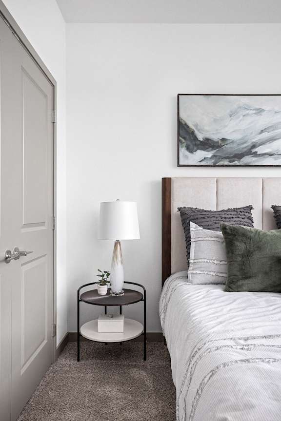 a small bedroom with a bed and a nightstand with a lamp and a painting  at Slate at Fishers District, Indiana