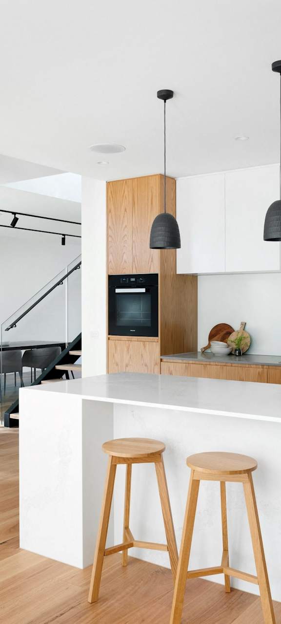 A kitchen with white cabinets and a white countertop with bar stools in front of it.