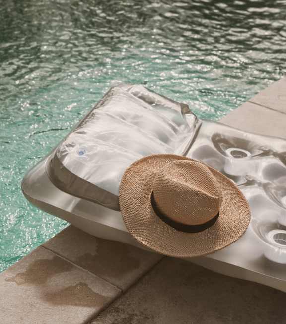 A hat is placed on a sun lounger by the pool.