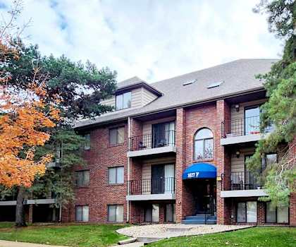 A red brick building with a blue awning and a tree with orange leaves in front.