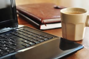 a cup of coffee next to a laptop computer on a desk
