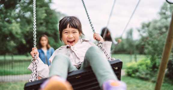 a young boy laughing on a swing in the park