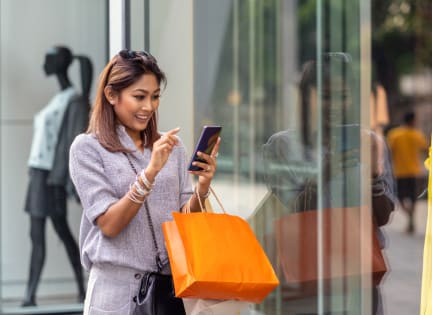 a woman looking at her cell phone while carrying a shopping bag