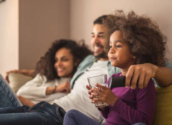 a young girl sitting on a couch holding a remote control
