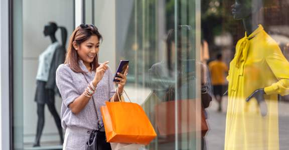 a woman looking at her cell phone while carrying a shopping bag