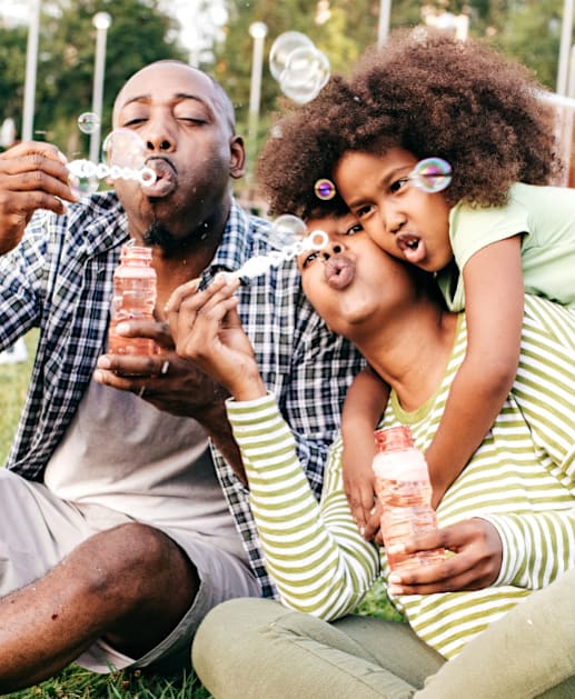 A family of three is sitting on the grass in a park.