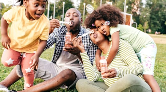 A family of three is sitting on the grass in a park.