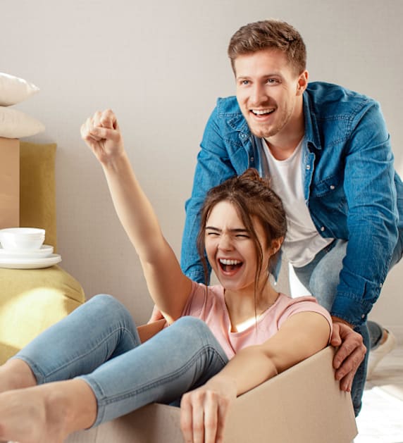 A man and a woman are excitedly sitting on the floor surrounded by moving boxes.
