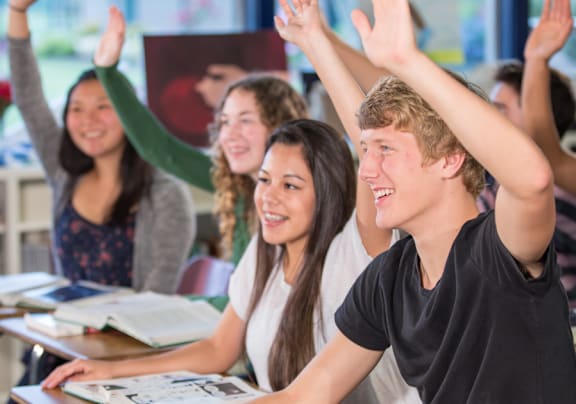A group of students raising their hands in a classroom.