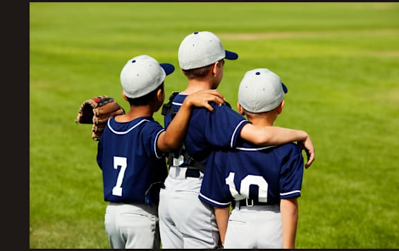 Three baseball players wearing blue jerseys hug each other on the field.