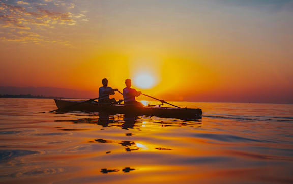 Two people rowing a boat on a calm body of water during sunset.