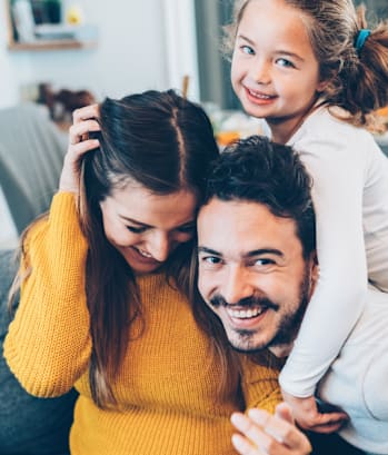 A family of three is sitting on a couch, with the child on the man's shoulders.