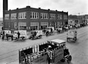 Thumbnail 2 of 8 - A black and white photo of a street with horse-drawn carriages and a building in the background.