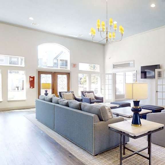 The community lounge with a couch, plush chairs, a TV, and coffee table at Harbin Pointe Apartments. 