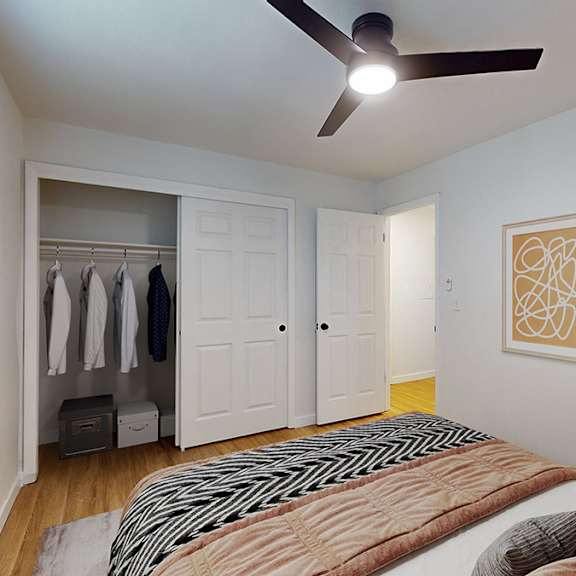 A bedroom with a bed, a ceiling fan, and a closet with clothes hanging.