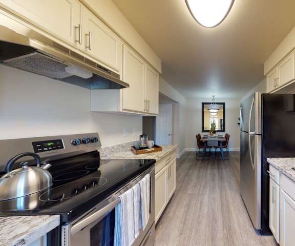 A large/cozy kitchen with stainless steel appliances, marble countertops, and large white wooden cabinets at Retreat at Austin Bluffs Apartment Homes. 