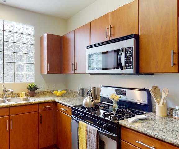 A large kitchen with stainless steel appliances, marble countertops with lots of room, yellow decorations, and large medium wooden cabinets at Vesada Apartment Homes. 