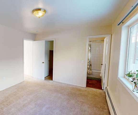 A large, empty carpeted bedroom with overhead lighting and a closet at the Village at Calais Apartment Homes. 