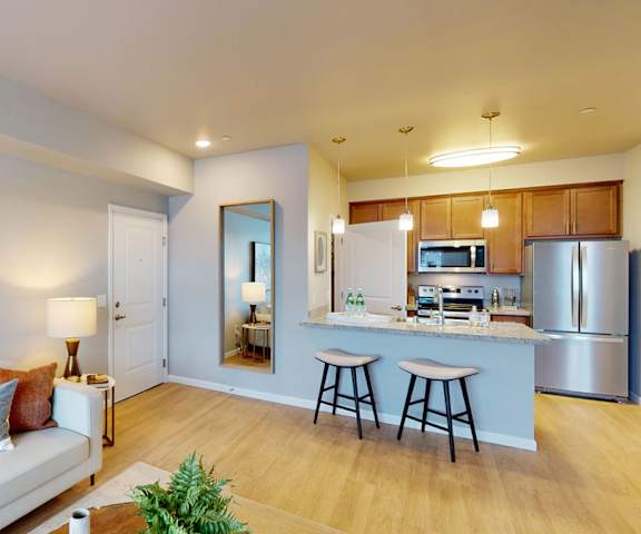 The living room with a couch, plush chairs, coffee table, decorations, a TV, and view of the dining room and the kitchen at LIVEasy Street Apartments. 