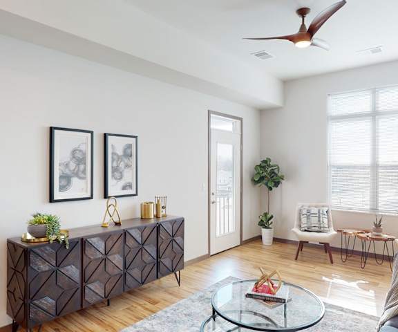 The spacious living room with a couch, throw pillows, large windows, a ceiling fan, wall art, plush chairs, coffee table, decorations, a TV, and large windows at Van Buren East Apartment Homes. 