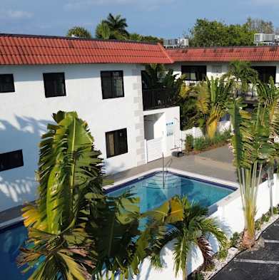 A white building with a red roof and a pool in the foreground.