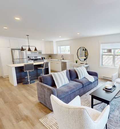 A modern living room with a grey sofa, white chairs, and a wooden floor.