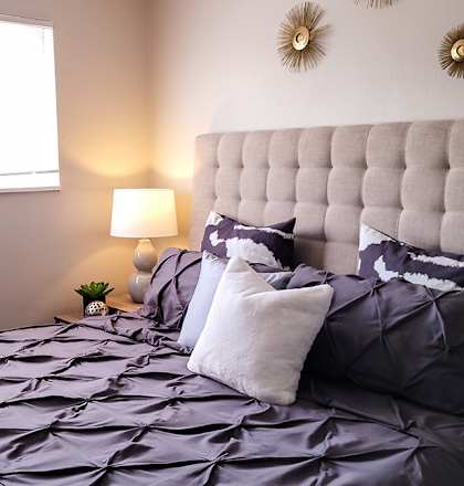 A bed with a grey comforter and pillows is in the image.