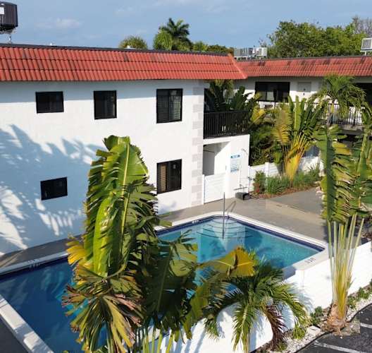 A white building with a pool surrounded by palm trees.